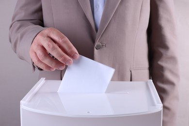 Photo of Man putting his vote into ballot box against light grey background, closeup