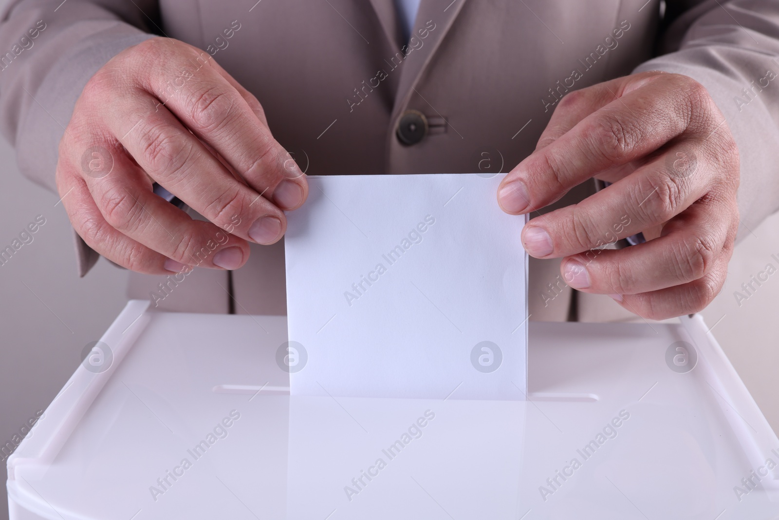 Photo of Man putting his vote into ballot box against light grey background, closeup