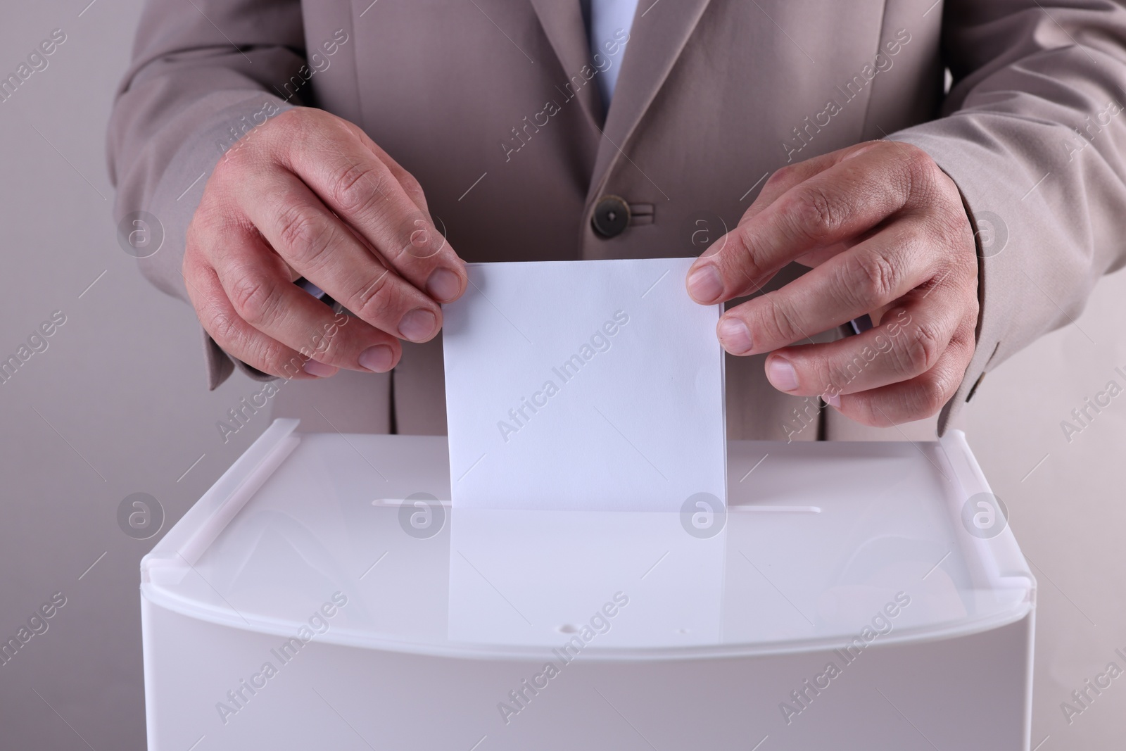 Photo of Man putting his vote into ballot box against light grey background, closeup