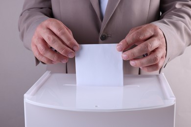 Man putting his vote into ballot box against light grey background, closeup