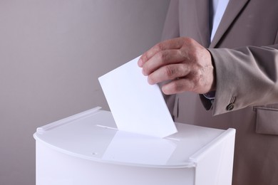 Photo of Man putting his vote into ballot box against light grey background, closeup