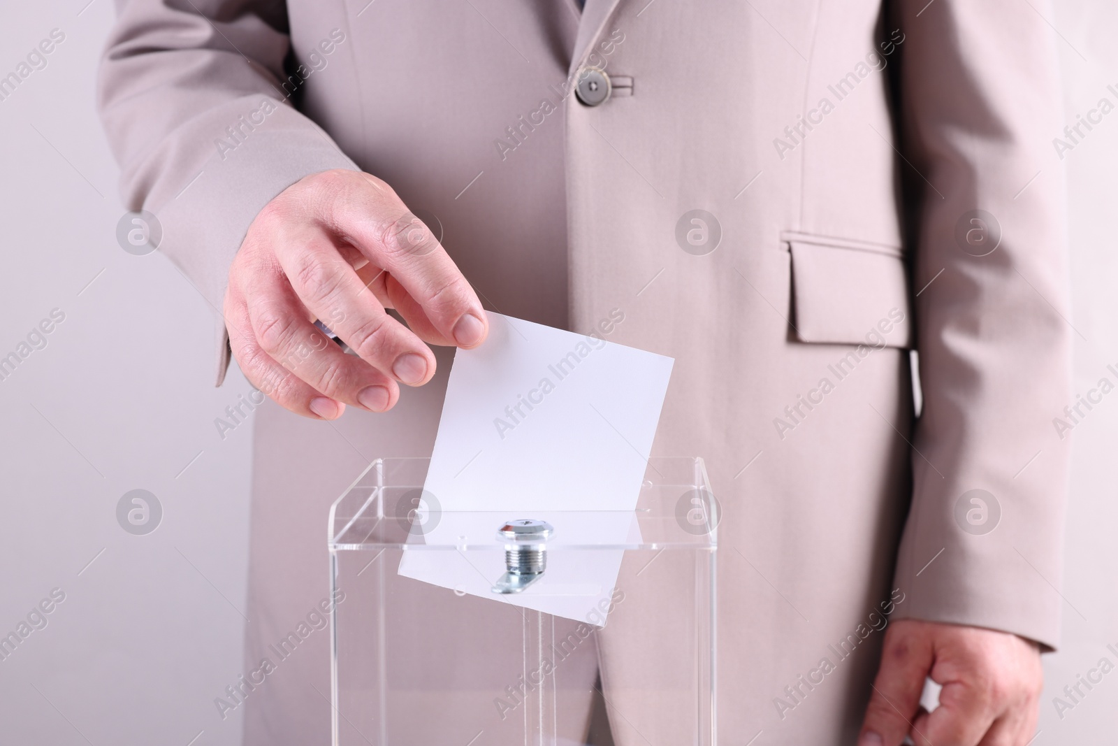 Photo of Man putting his vote into ballot box against light grey background, closeup