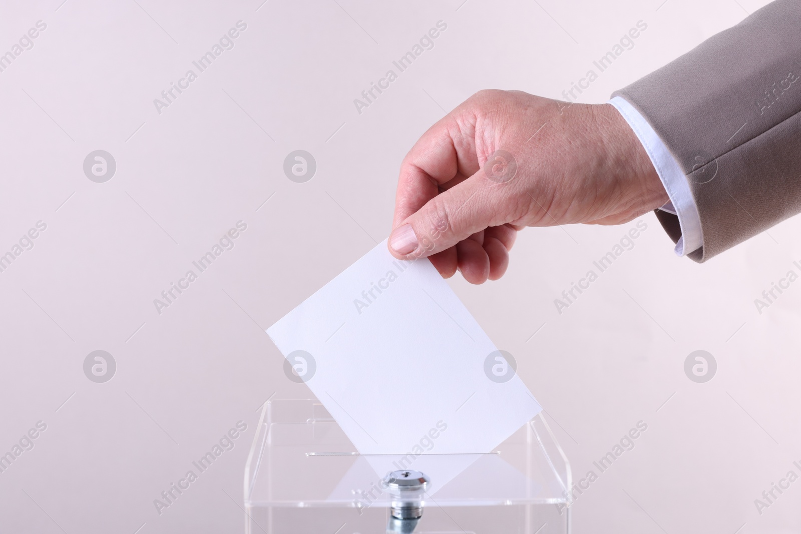 Photo of Man putting his vote into ballot box against light grey background, closeup