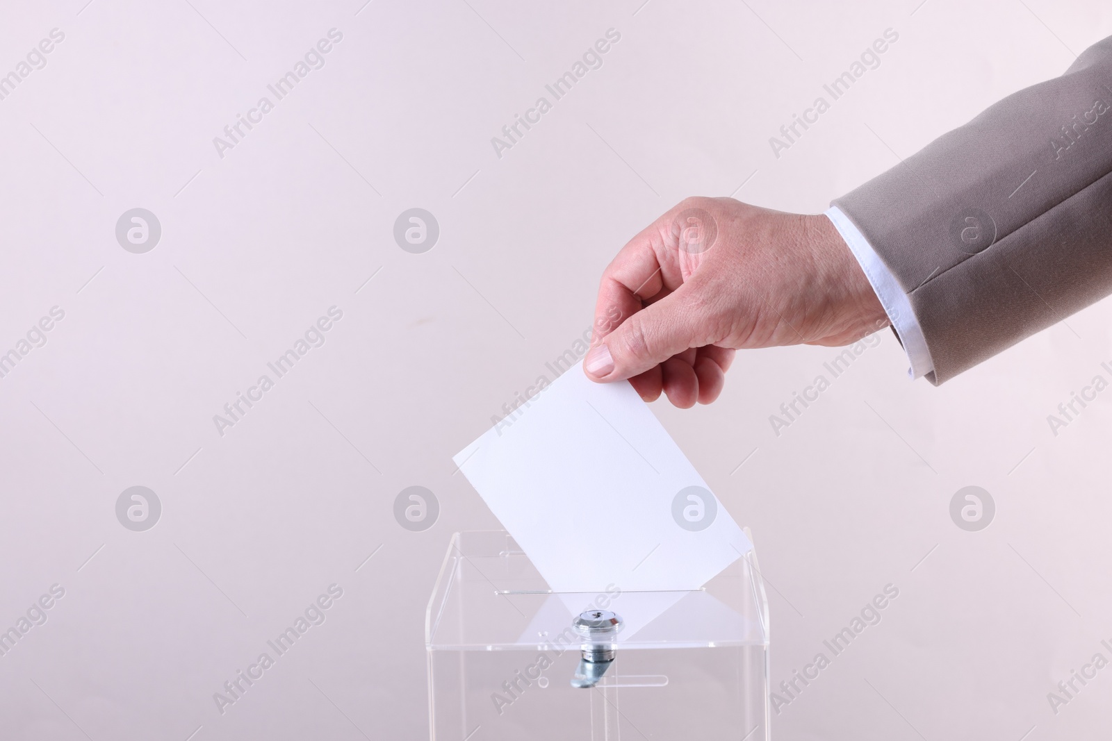 Photo of Man putting his vote into ballot box against light grey background, closeup. Space for text