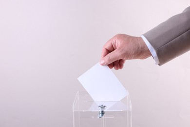 Photo of Man putting his vote into ballot box against light grey background, closeup. Space for text