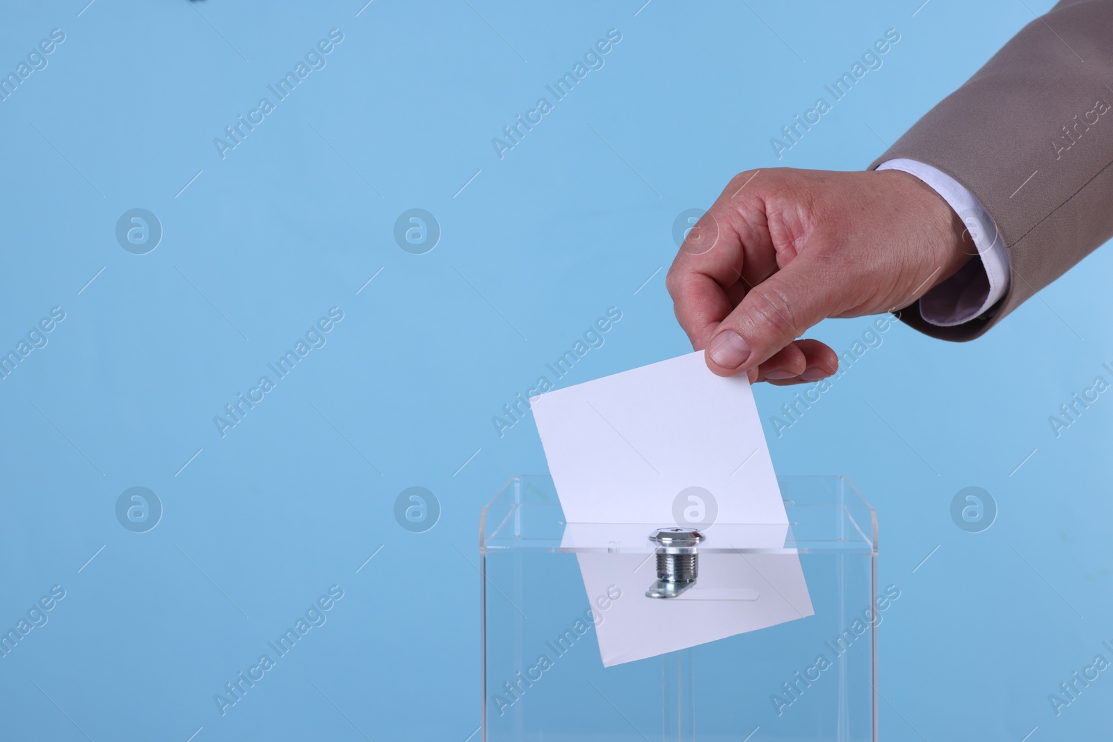 Photo of Man putting his vote into ballot box against light blue background, closeup. Space for text