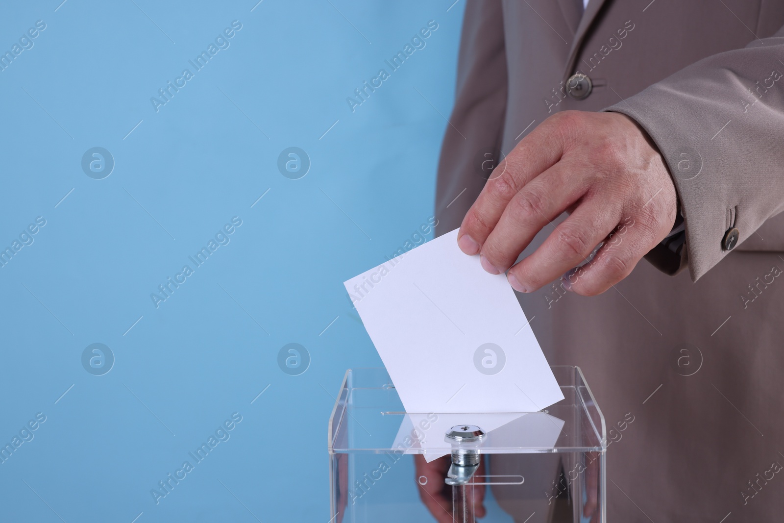 Photo of Man putting his vote into ballot box against light blue background, closeup. Space for text