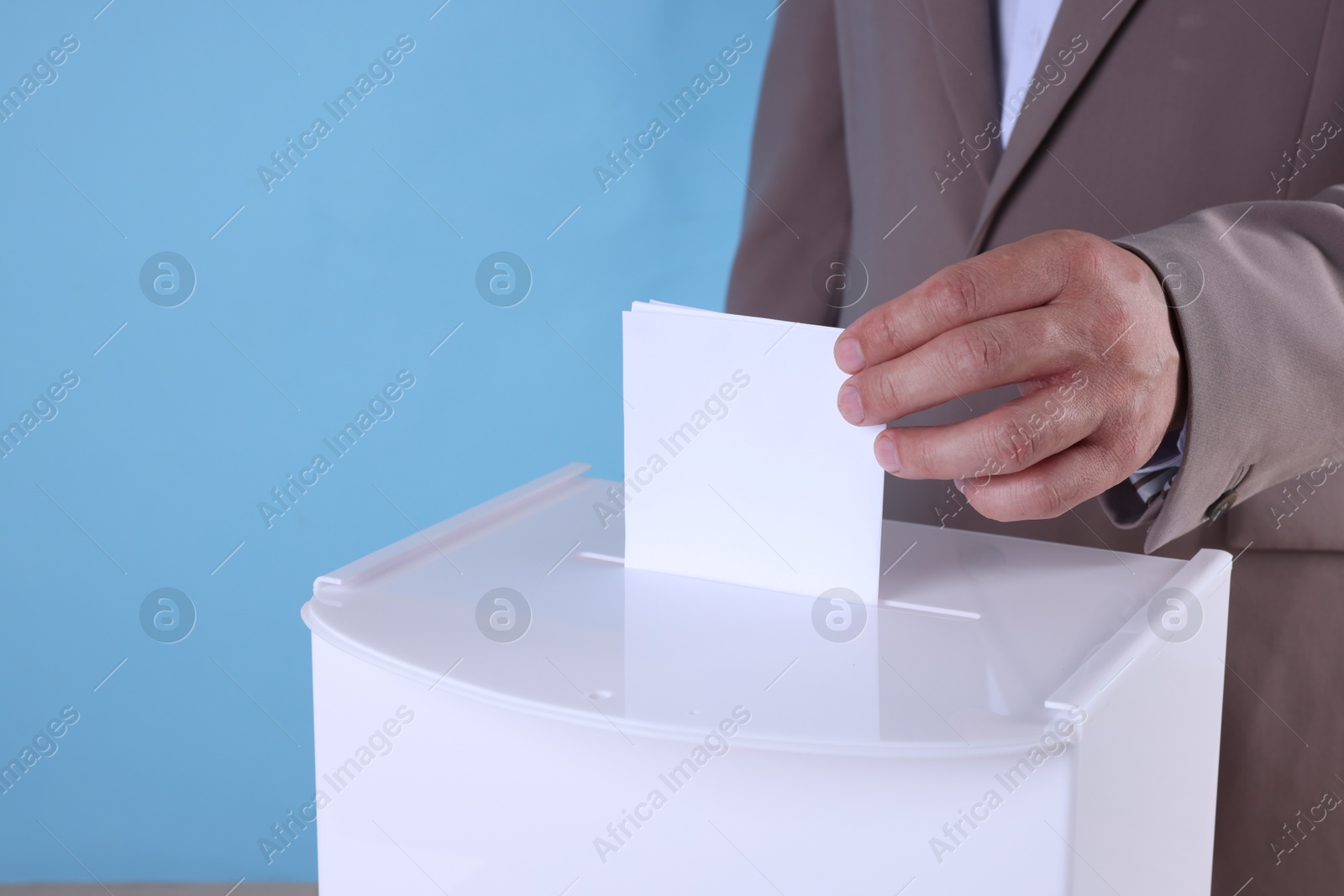 Photo of Man putting his vote into ballot box against light blue background, closeup. Space for text