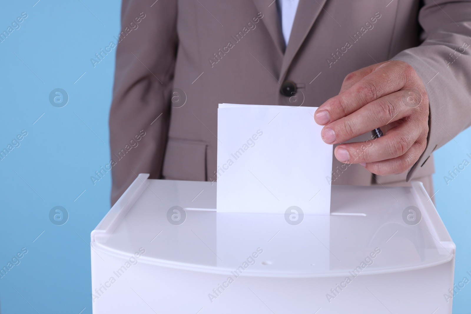 Photo of Man putting his vote into ballot box against light blue background, closeup