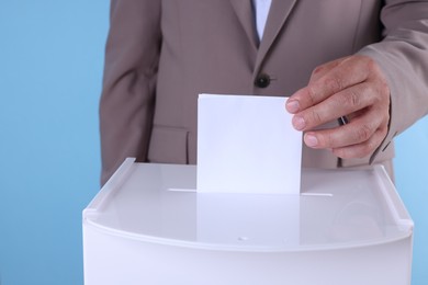 Photo of Man putting his vote into ballot box against light blue background, closeup