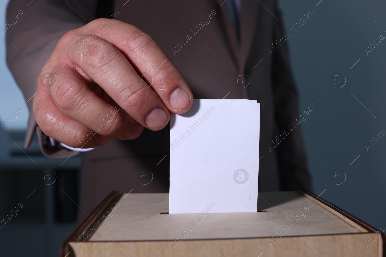 Photo of Man putting his vote into ballot box indoors, closeup