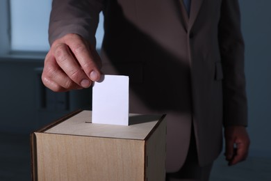 Photo of Man putting his vote into ballot box indoors, closeup