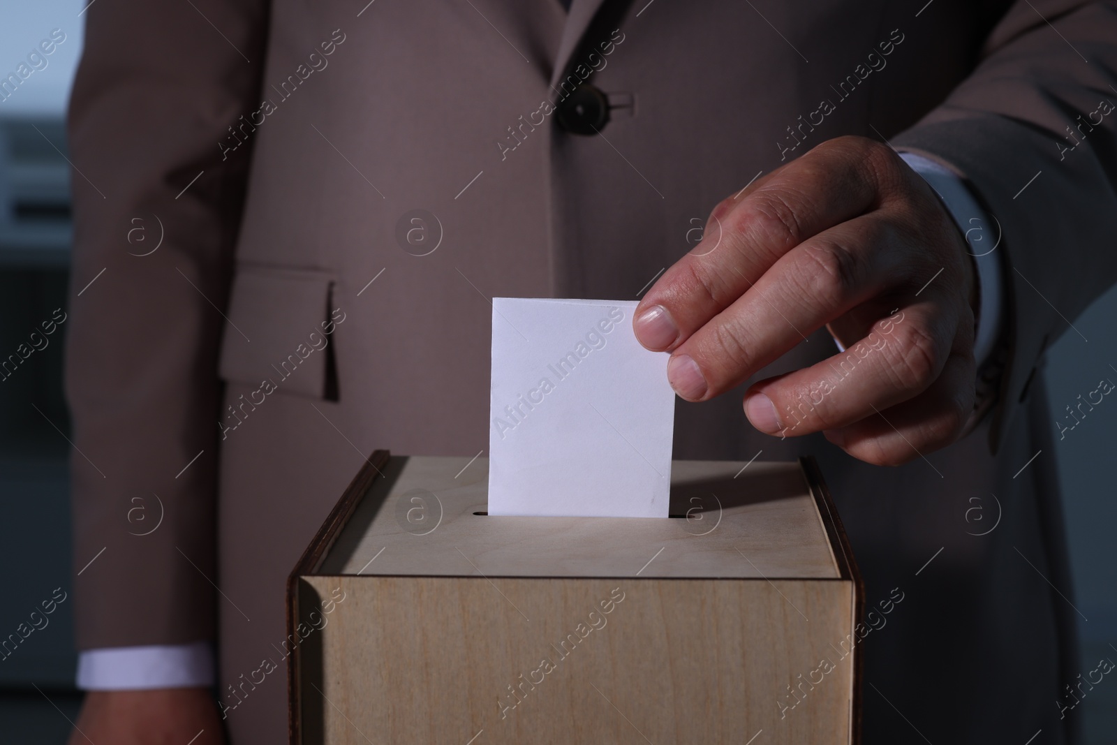 Photo of Man putting his vote into ballot box indoors, closeup