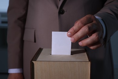 Photo of Man putting his vote into ballot box indoors, closeup