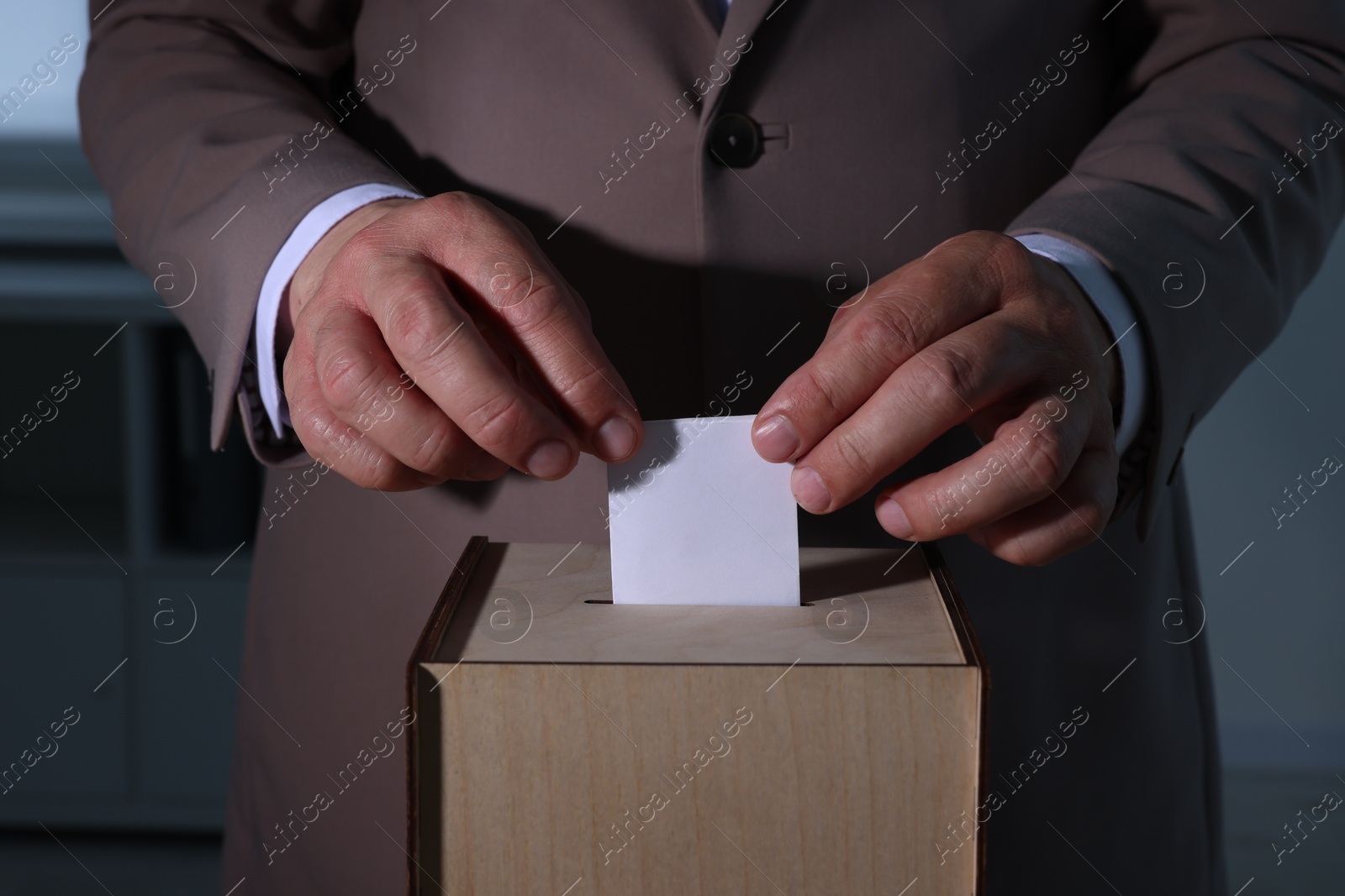 Photo of Man putting his vote into ballot box indoors, closeup