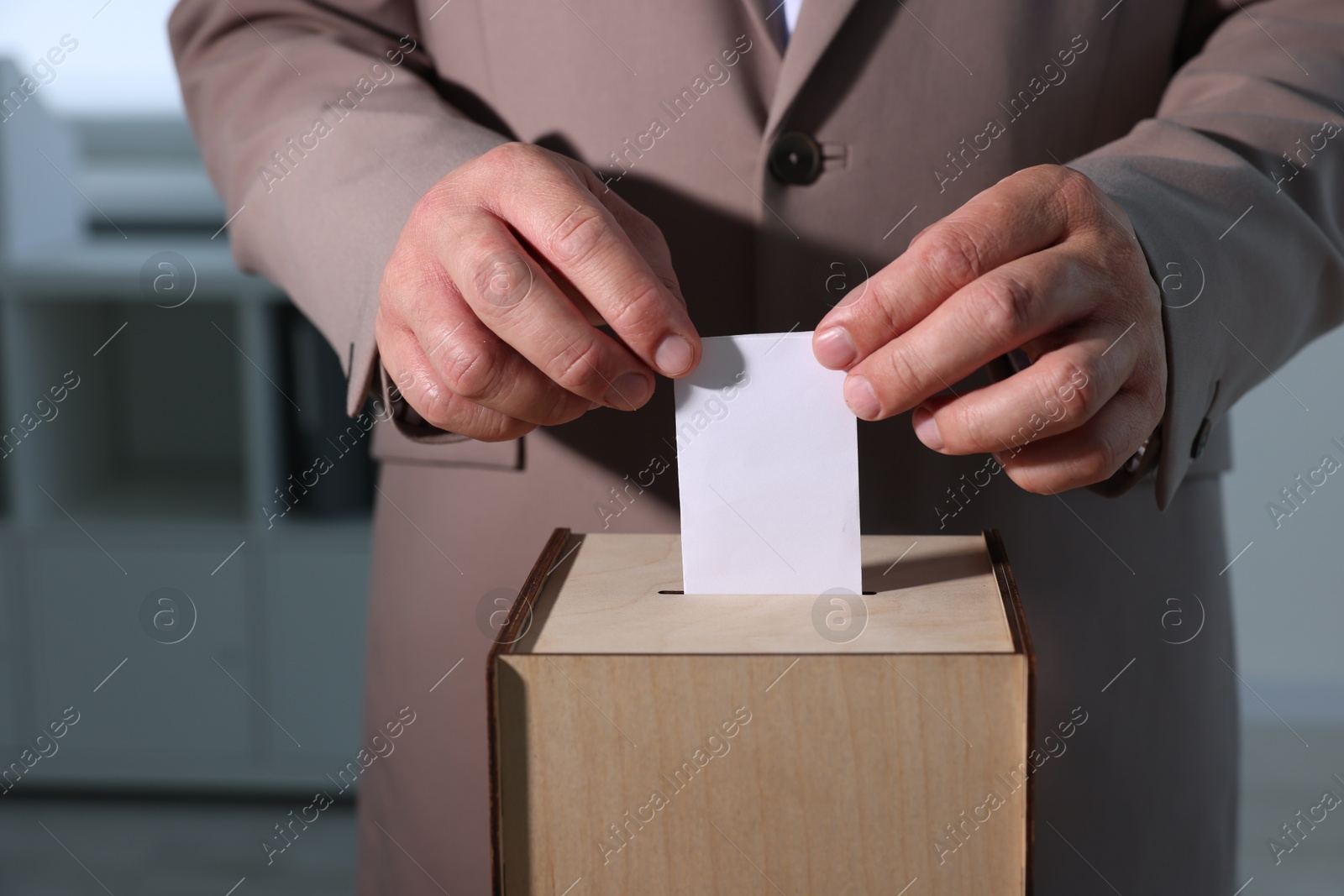 Photo of Man putting his vote into ballot box indoors, closeup