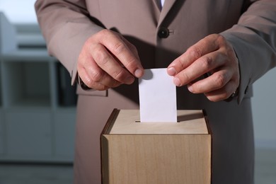 Man putting his vote into ballot box indoors, closeup