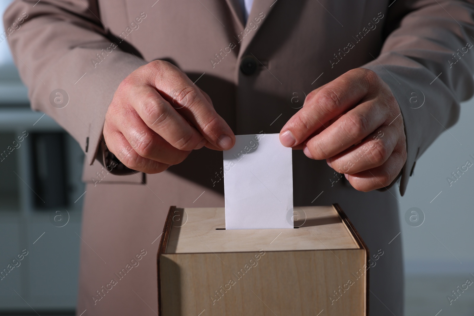 Photo of Man putting his vote into ballot box indoors, closeup