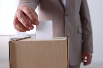 Photo of Man putting his vote into ballot box indoors, closeup