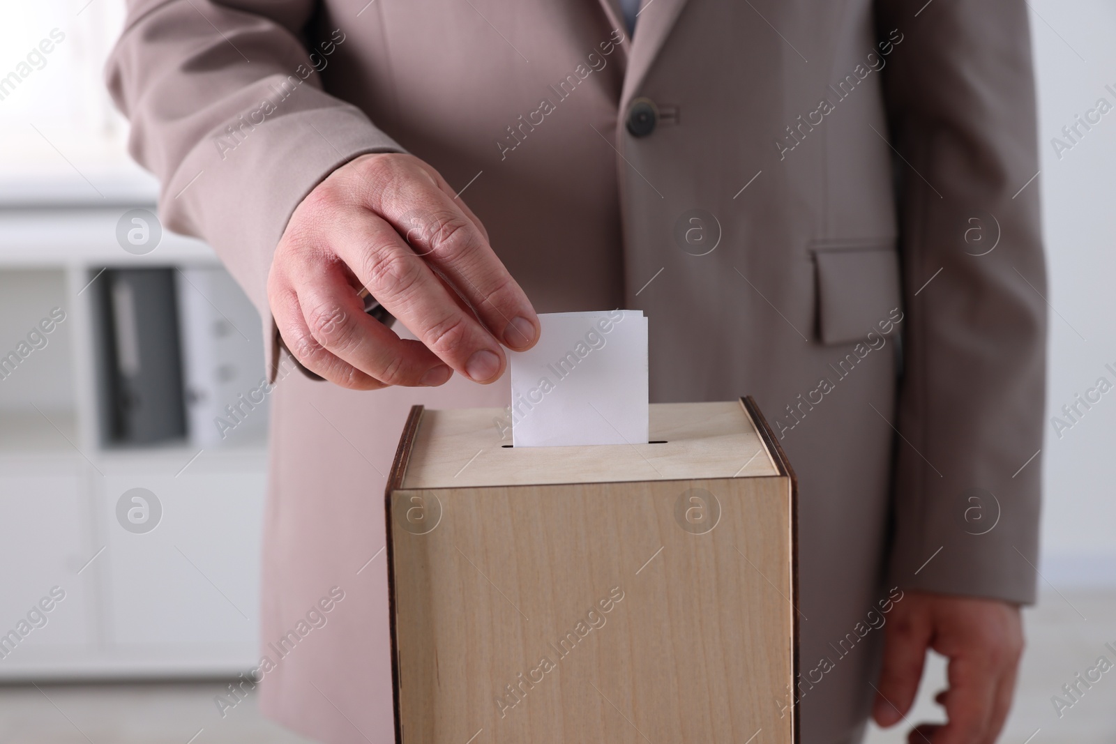 Photo of Man putting his vote into ballot box indoors, closeup