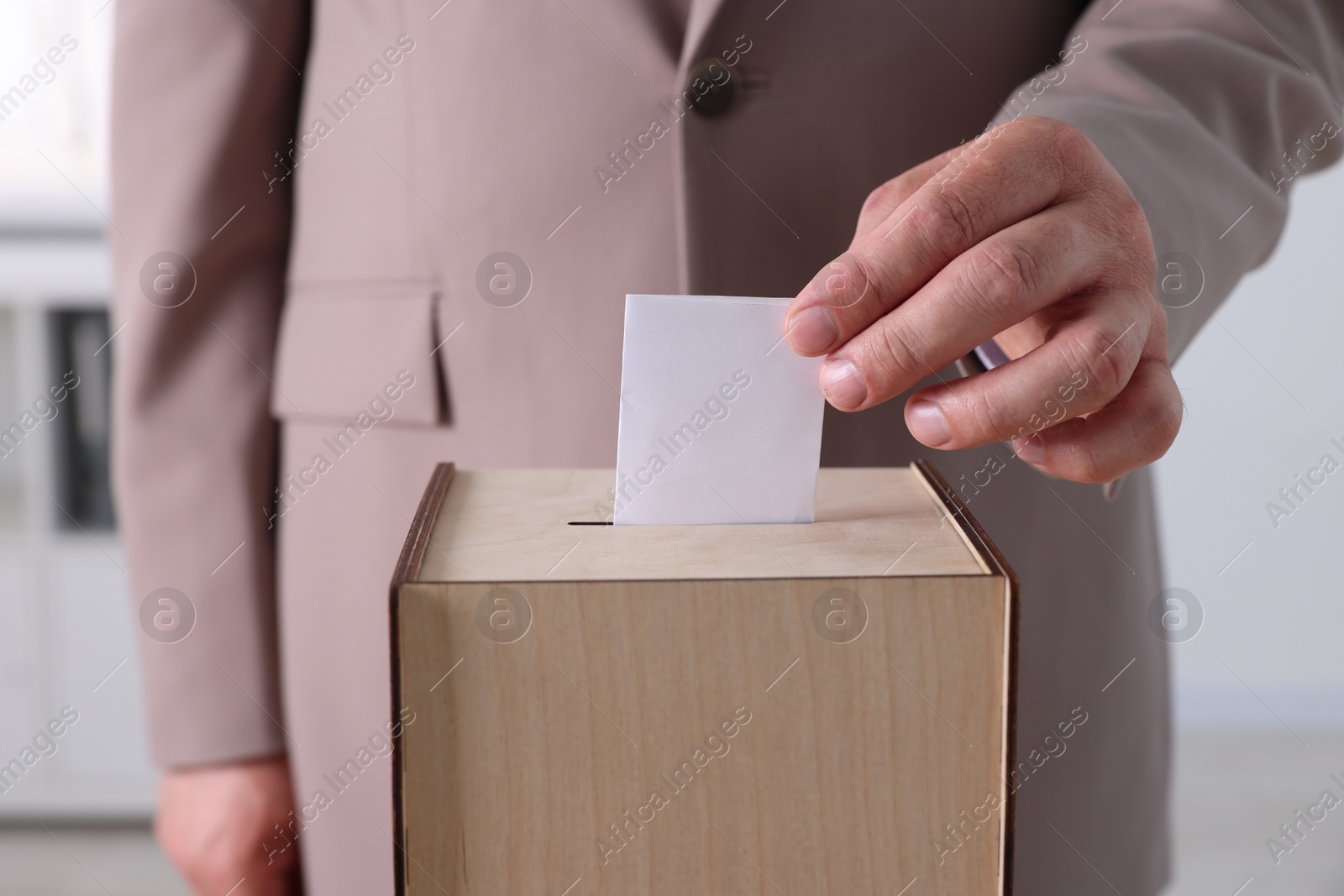 Photo of Man putting his vote into ballot box indoors, closeup