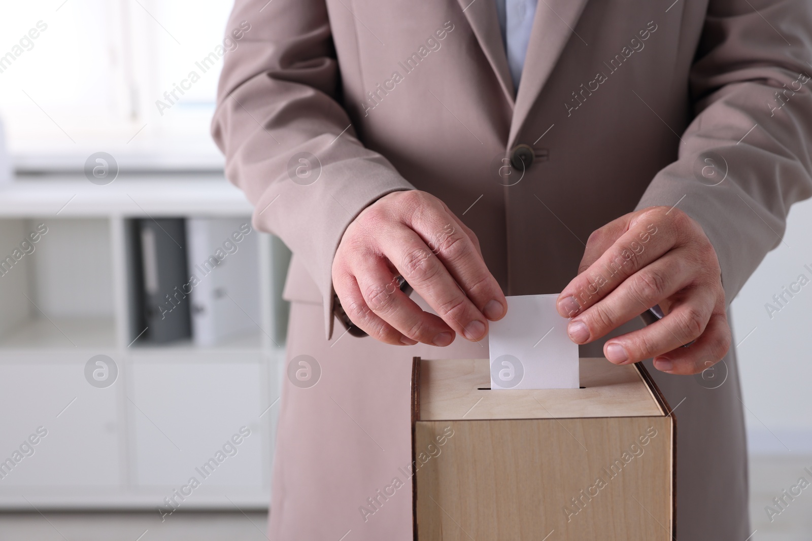 Photo of Man putting his vote into ballot box indoors, closeup