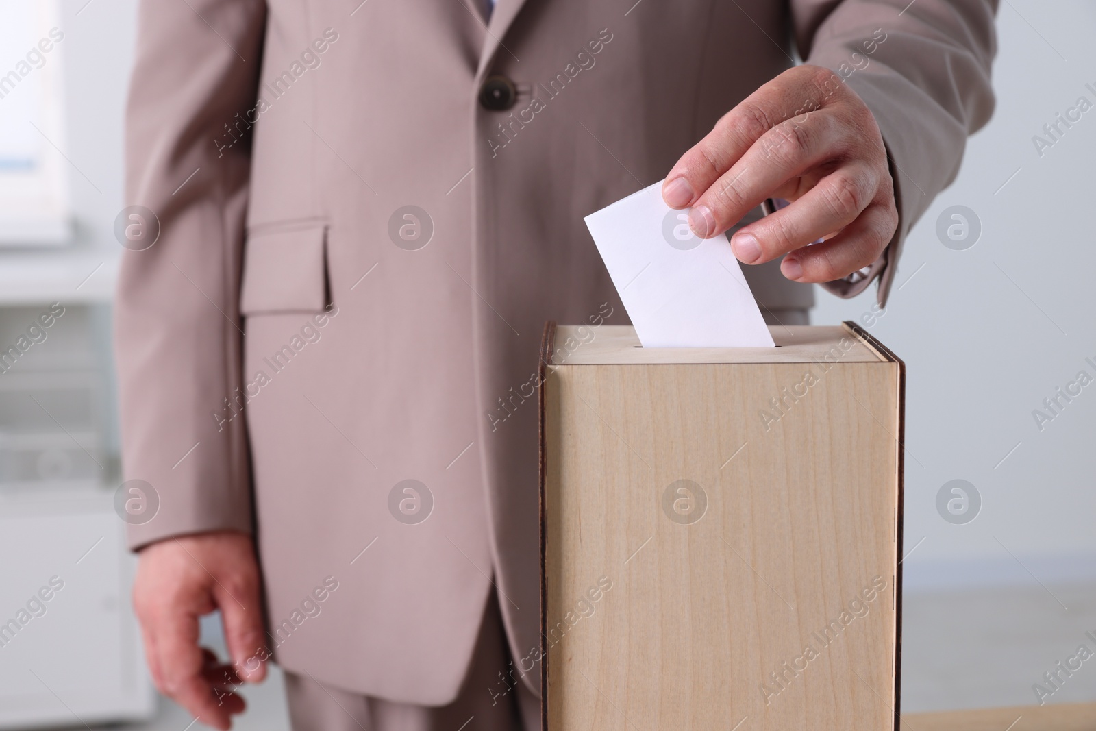 Photo of Man putting his vote into ballot box indoors, closeup