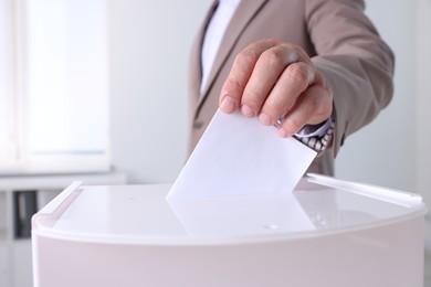 Photo of Man putting his vote into ballot box indoors, closeup