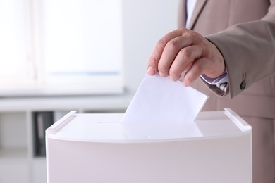 Man putting his vote into ballot box indoors, closeup. Space for text