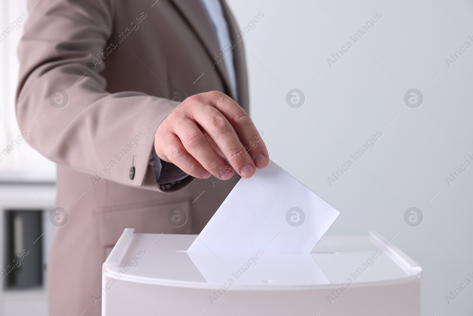 Photo of Man putting his vote into ballot box indoors, closeup