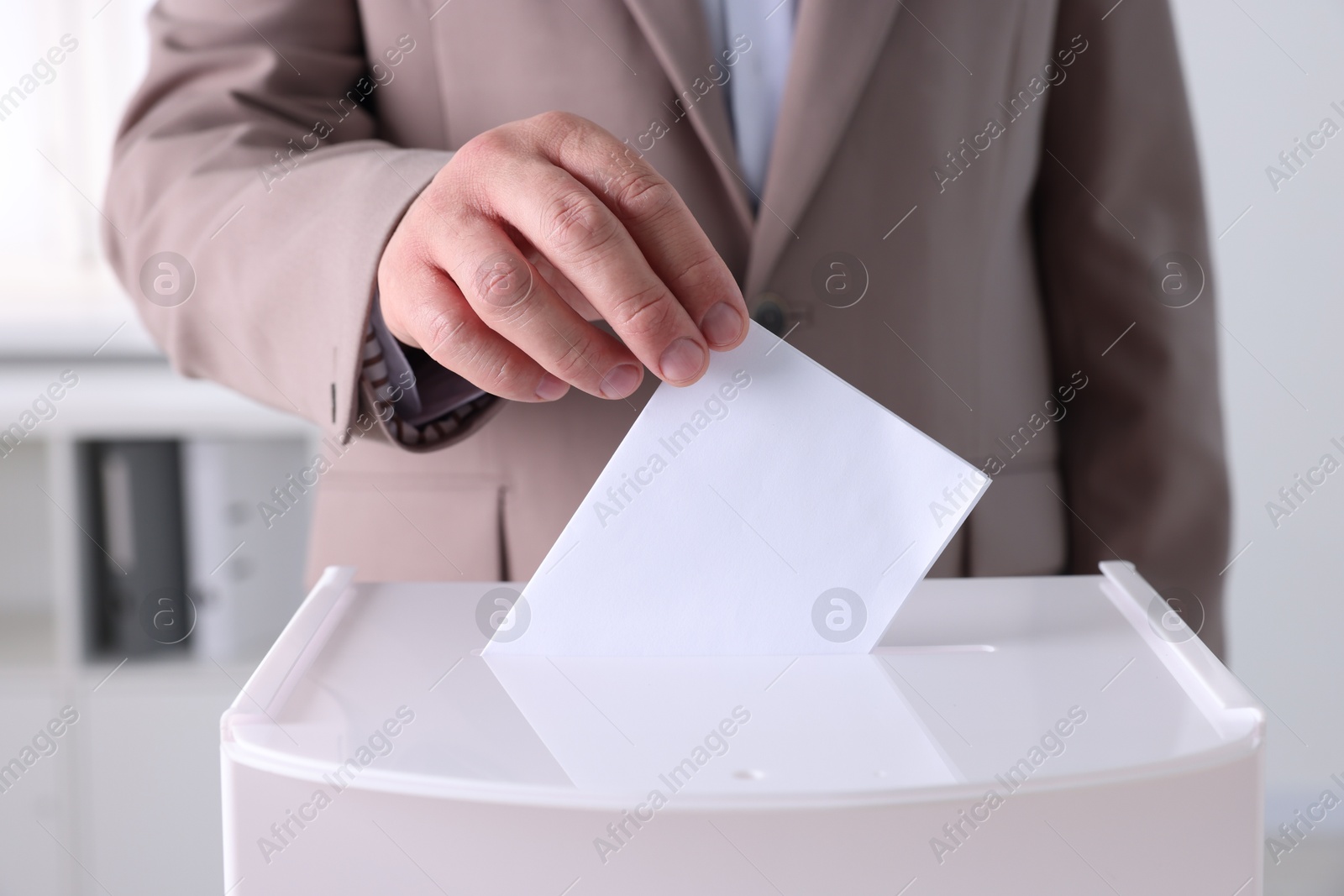 Photo of Man putting his vote into ballot box indoors, closeup