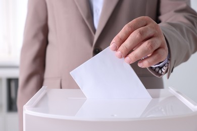 Photo of Man putting his vote into ballot box indoors, closeup