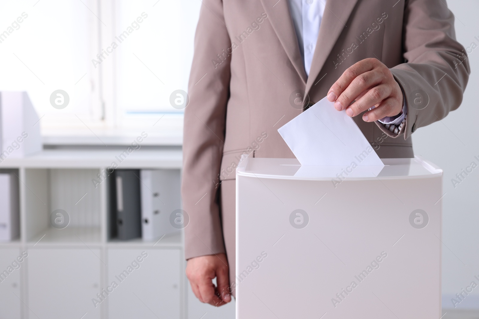 Photo of Man putting his vote into ballot box indoors, closeup