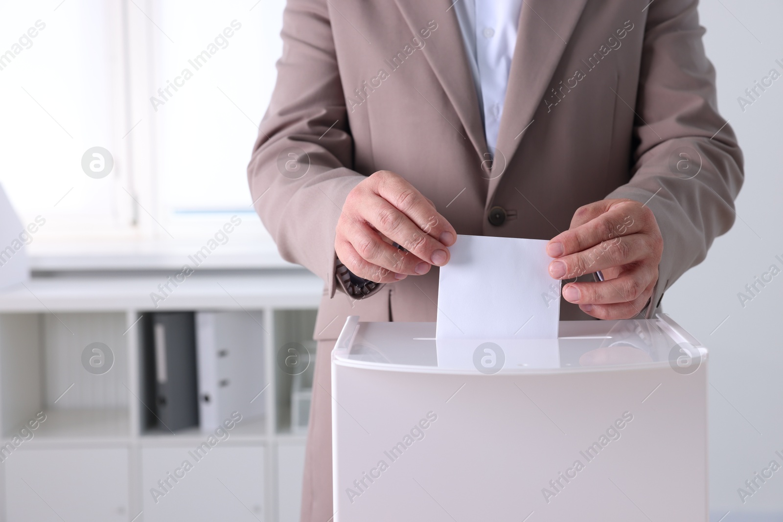 Photo of Man putting his vote into ballot box indoors, closeup