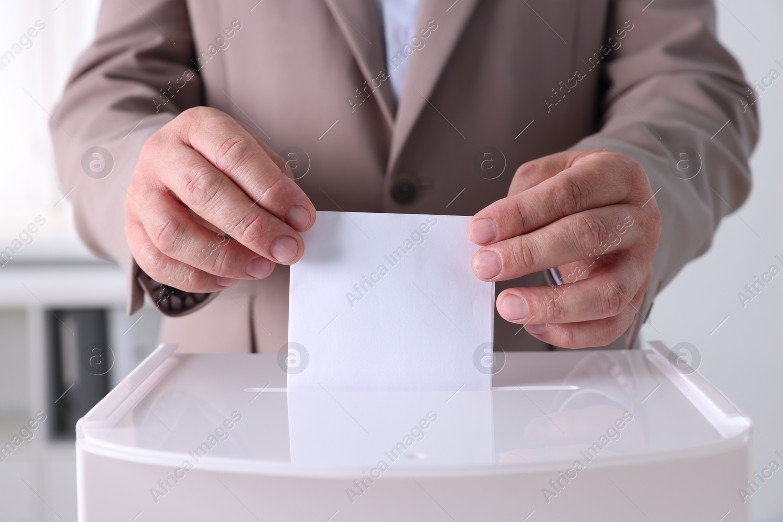 Photo of Man putting his vote into ballot box indoors, closeup