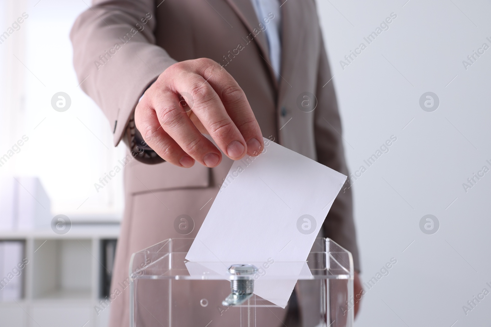 Photo of Man putting his vote into ballot box indoors, closeup