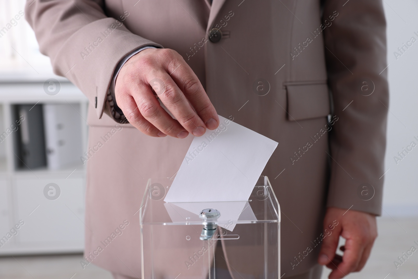 Photo of Man putting his vote into ballot box indoors, closeup