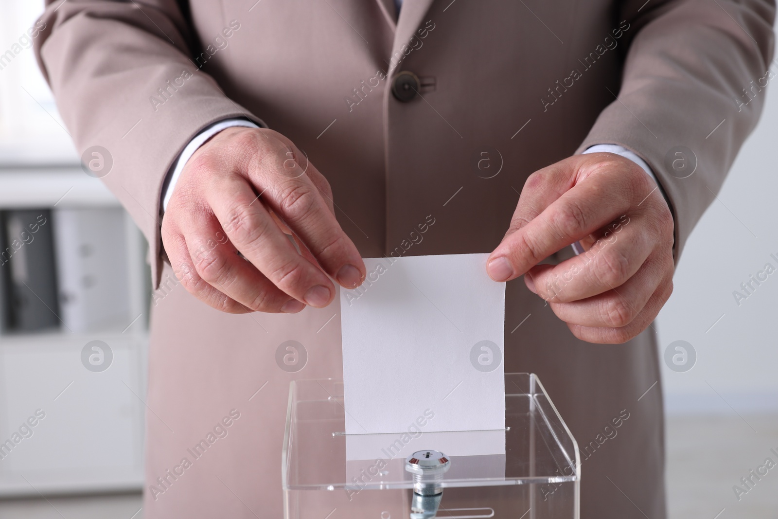 Photo of Man putting his vote into ballot box indoors, closeup