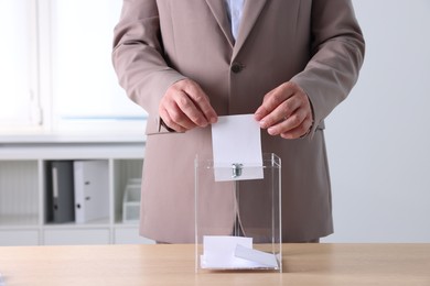 Photo of Man putting his vote into ballot box at wooden table indoors, closeup