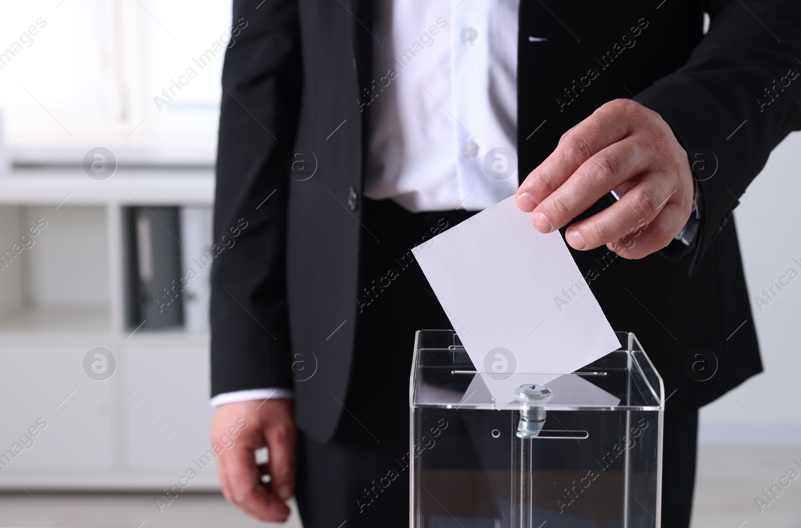 Photo of Man putting his vote into ballot box indoors, closeup