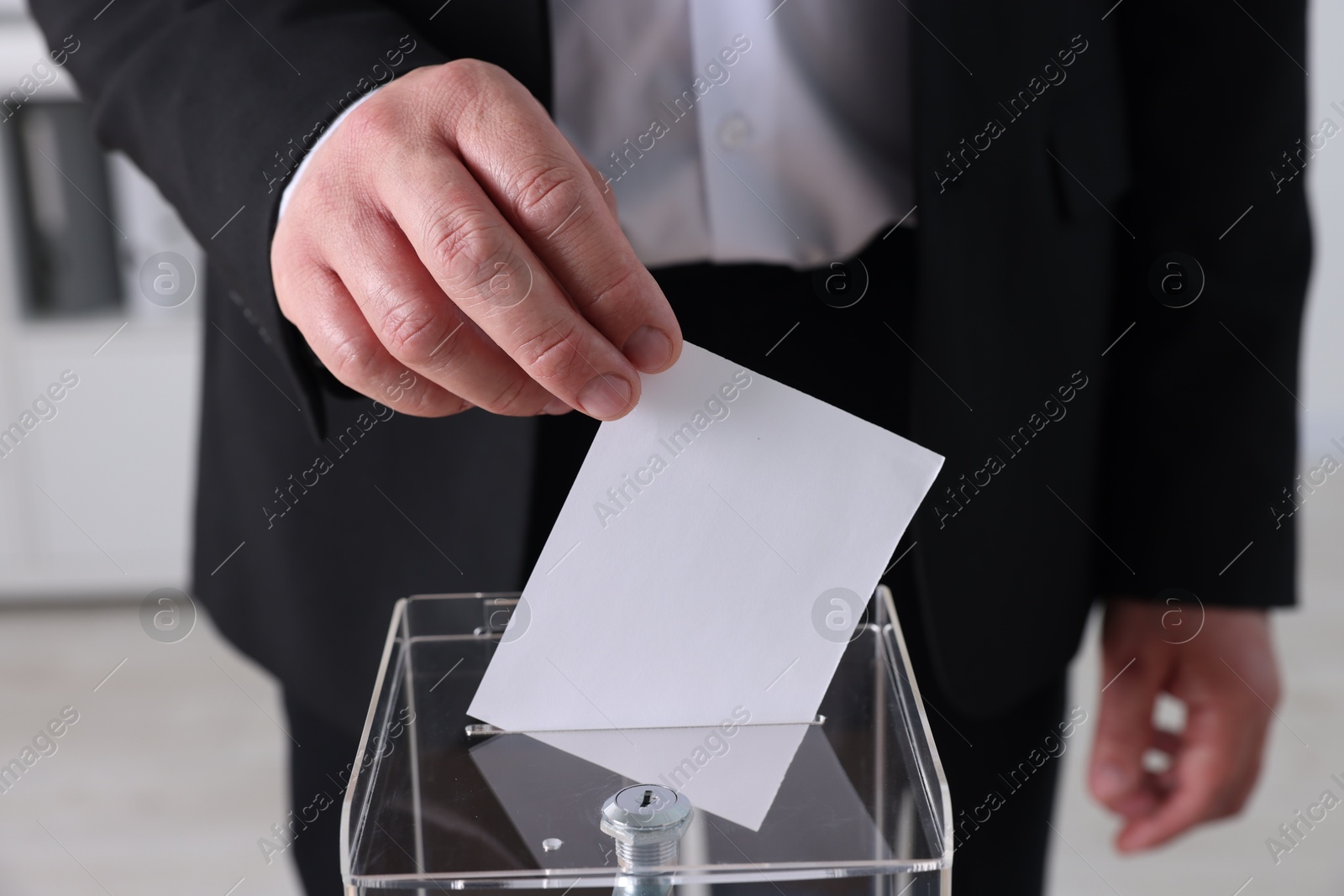 Photo of Man putting his vote into ballot box indoors, closeup