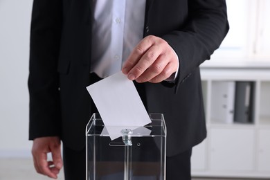 Photo of Man putting his vote into ballot box indoors, closeup