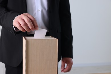 Man putting his vote into ballot box indoors, closeup. Space for text