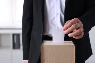 Photo of Man putting his vote into ballot box indoors, closeup