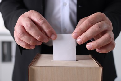 Photo of Man putting his vote into ballot box indoors, closeup