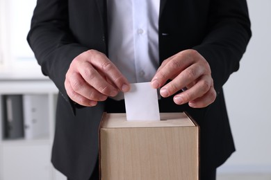 Photo of Man putting his vote into ballot box indoors, closeup