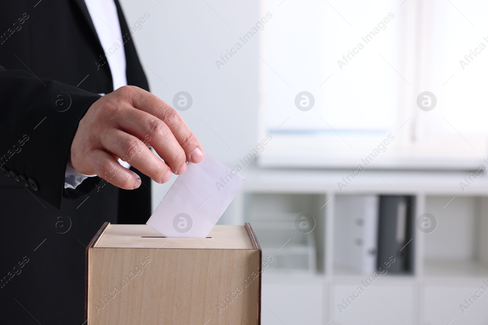 Photo of Man putting his vote into ballot box indoors, closeup. Space for text