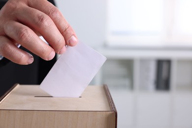 Photo of Man putting his vote into ballot box indoors, closeup. Space for text