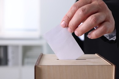 Photo of Man putting his vote into ballot box indoors, closeup