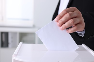 Photo of Man putting his vote into ballot box indoors, closeup